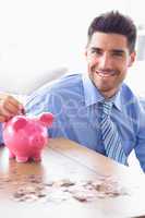 Handsome businessman putting coins into piggy bank looking at ca