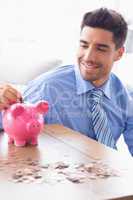 Handsome businessman putting change into piggy bank