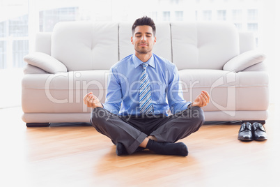Businessman meditating in lotus pose on the floor