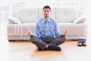 Businessman meditating in lotus pose on the floor