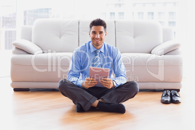 Businessman sitting on floor using tablet pc smiling at camera