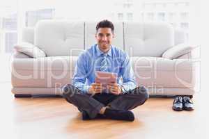 Businessman sitting on floor using tablet pc smiling at camera