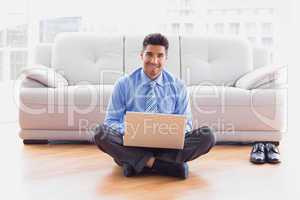 Businessman sitting on floor using laptop smiling at camera