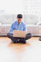 Happy businessman sitting on floor using his laptop