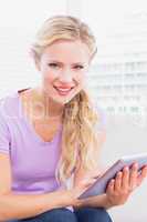 Smiling blonde sitting on her sofa using her tablet pc