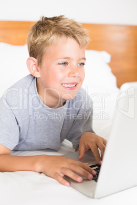 Blonde boy lying on bed using laptop
