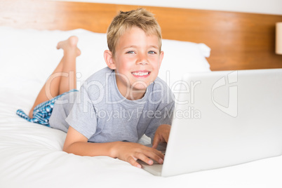 Happy blonde boy lying on bed using laptop