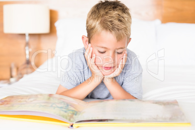 Happy blonde boy lying on bed reading a storybook