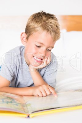 Cute blonde boy lying on bed reading a storybook