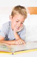 Cute blonde boy lying on bed reading a storybook