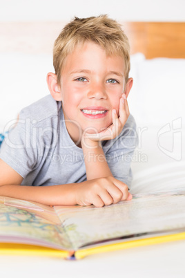 Cheerful blonde boy lying on bed reading a storybook