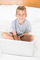 Cute blonde boy sitting on bed using laptop