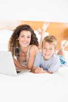 Cute blonde boy and mother lying on bed using laptop
