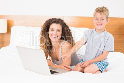 Happy blonde boy and mother on bed using laptop