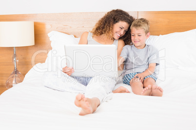 Mother and son sitting on bed using laptop Mother and son sitting on bed using laptop