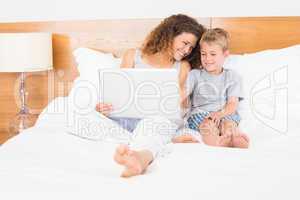 Mother and son sitting on bed using laptop