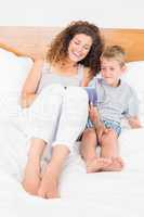 Happy mother and son sitting on bed with tablet pc