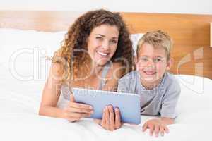 Happy mother and son lying on bed with tablet pc