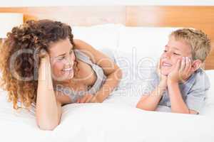 Happy mother and son lying on bed facing each other