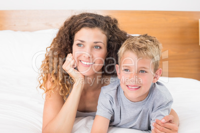 Happy mother and son lying on bed looking away