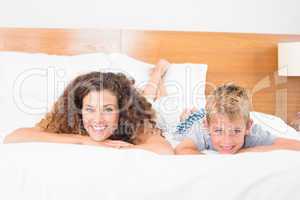 Smiling mother and son lying on bed looking at camera
