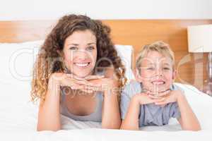 Cheerful mother and son lying on bed looking at camera