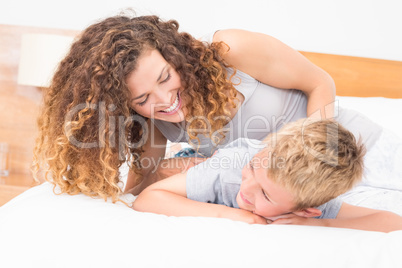 Happy mother tickling her son on bed