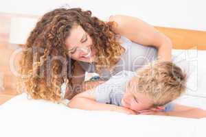Happy mother tickling her son on bed