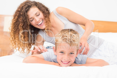 Happy mother tickling her cute son on bed