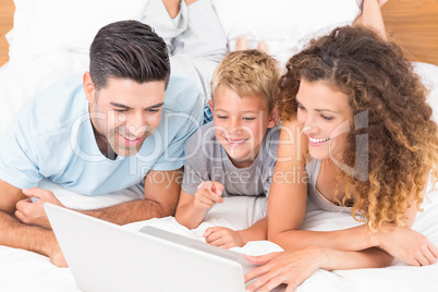 Smiling young family using laptop together on bed