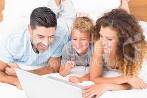Smiling young family using laptop together on bed