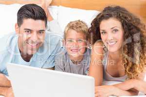 Happy young family using laptop together on bed