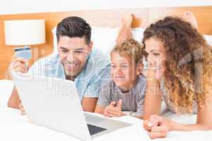 Happy young family using laptop to shop online together on bed