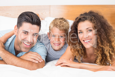 Smiling young family lying on bed looking at camera