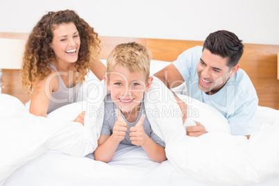 Cute young family messing about on bed with little boy showing t