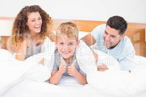 Cute young family messing about on bed with little boy showing t