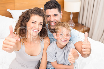 Happy young family smiling at camera on bed giving thumbs up