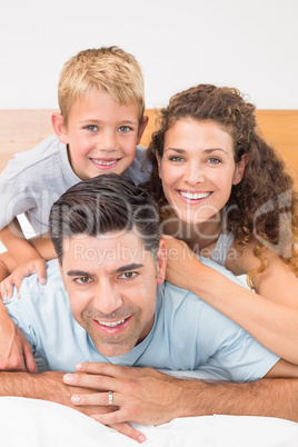 Attractive young family smiling at camera on bed posing