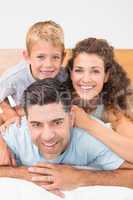 Attractive young family smiling at camera on bed posing