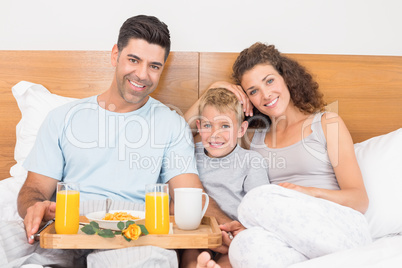 Happy young family having breakfast in bed