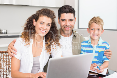 Happy little boy using laptop with parents at table