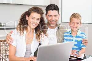Happy little boy using laptop with parents at table