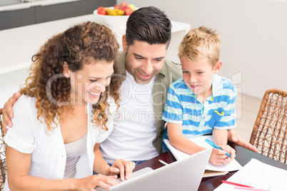 Cute little boy using laptop with his parents at table