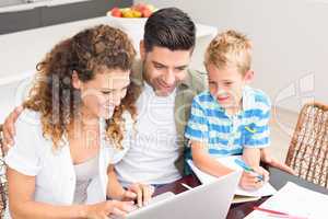 Cute little boy using laptop with his parents at table