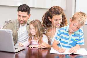 Cheerful parents colouring and using laptop with their children