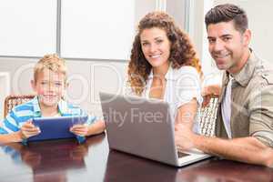 Happy parents sitting with son using tablet and laptop