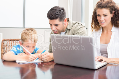 Father and son colouring with mother using laptop