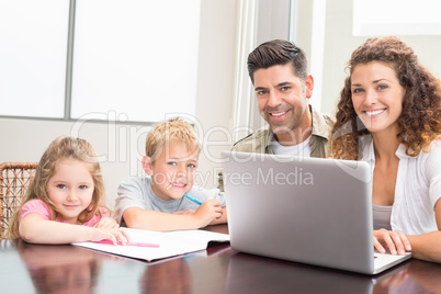Family sitting at table with laptop and colouring book