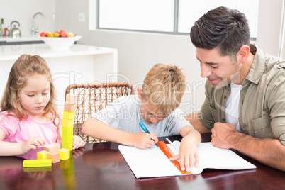 Father helping son with homework with little girl playing with b