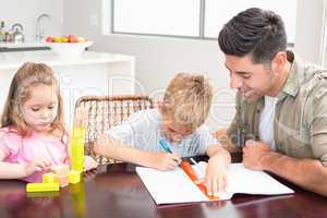 Father helping son with homework with little girl playing with b
